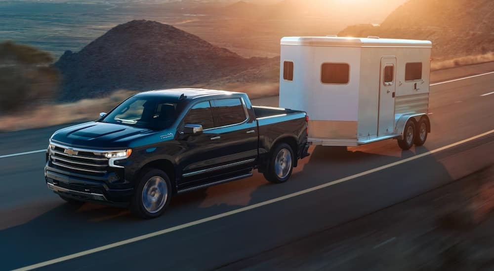 A black 2024 Chevy Silverado 1500 High Country is shown towing a trailer.
