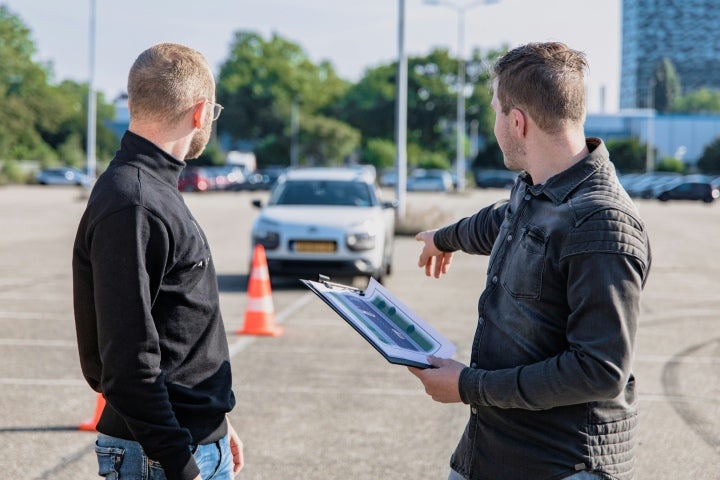 Two driving instructors pointing to car.