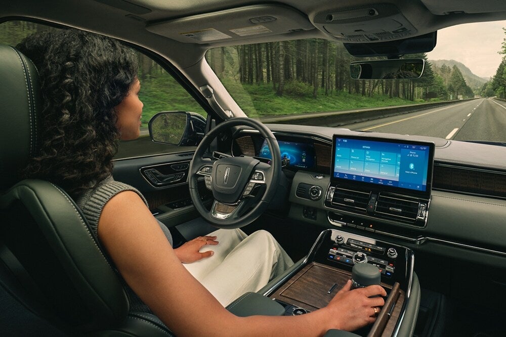 Woman driving a Lincoln navigator, showcasing the interior console and touchscreen. 