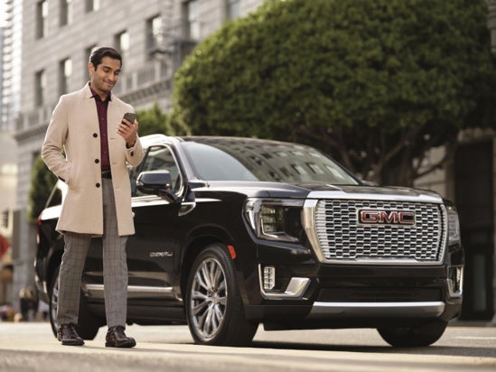 Man looking at phone standing next to 2025 GMC Denali