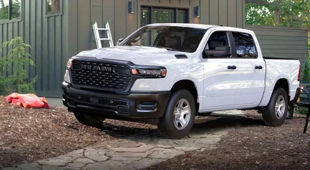 A white 2025 Ram 1500 parked in front of a forest home