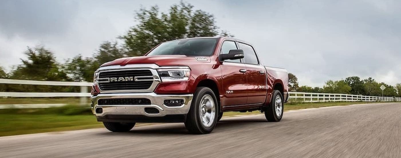 A red 2020 Ram 1500 driving near white fence.