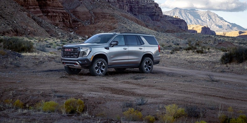 Silver GMC Yukon SUV parked on a rugged desert trail with mountains in the background.