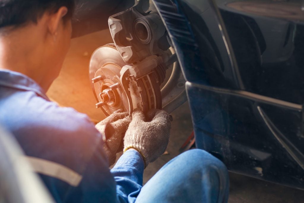 Automotive technician inspecting and repairing a vehicle brake system at a service shop.