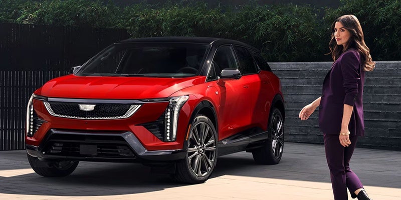 Woman walking beside a red Cadillac SUV in an outdoor setting.