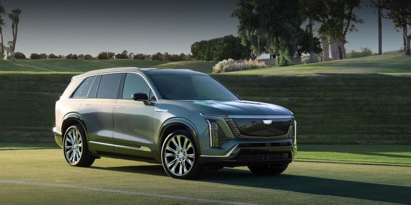 Gray Cadillac electric crossover SUV on grassy landscape.