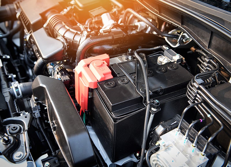 Car battery and engine bay components under the hood of a vehicle.