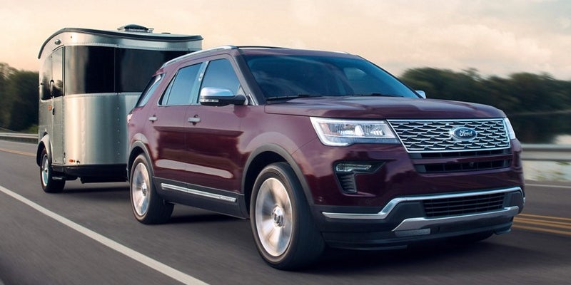 A maroon Ford Explorer SUV towing a gleaming silver Airstream trailer down a highway at dusk.