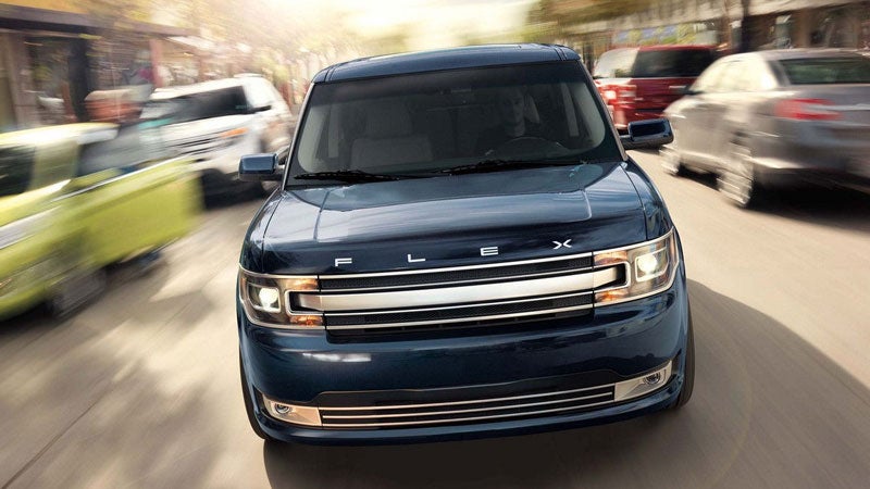 Front view of a dark blue Ford Flex driving on a street, with other blurred cars suggesting movement.