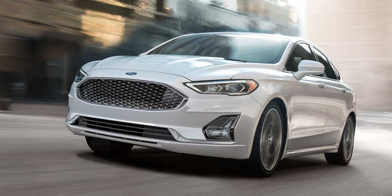 A shiny silver sedan drives forward, angled slightly to the left. The background is blurred to show motion.