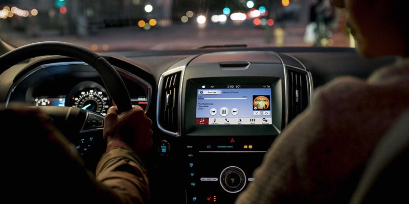 Interior view of a car at night showing driver's hands on the steering wheel and the touchscreen audio system.