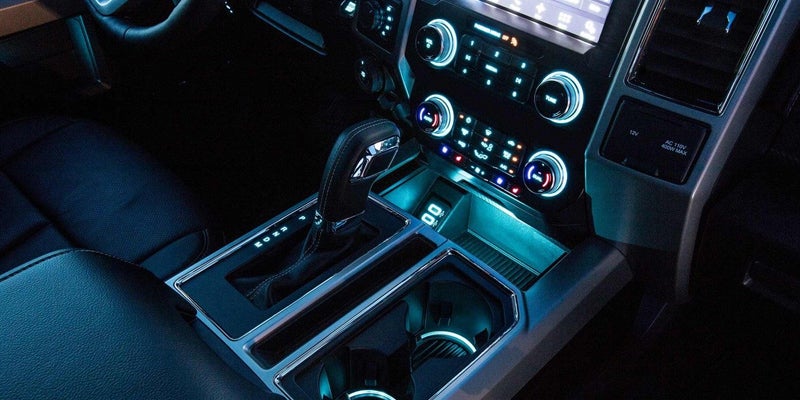 Car interior, focusing on the center console with blue ambient lighting, gear shift, infotainment, and climate controls.