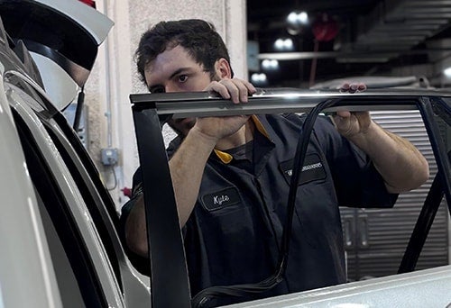 A mechanic named Kyle installs a new window in the door of a white car.