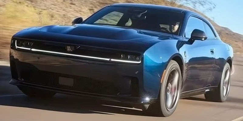 Front-side view of a glossy dark blue Dodge Charger driving on a road.