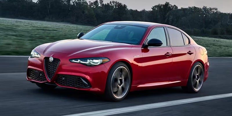 A shiny red Alfa Romeo Giulia parked on a road with trees in the background.