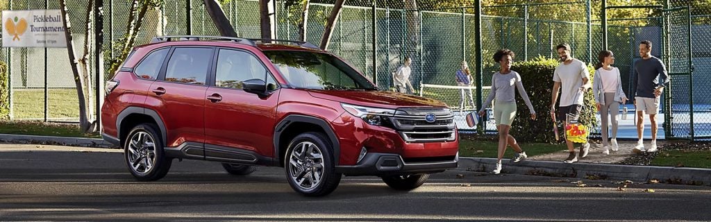 A red Subaru Forester parked near a pickleball court with people walking by