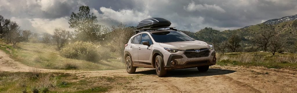 A Subaru Crosstrek driving on a dirt road with a mountain backdrop
