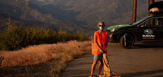 Woman in safety vest picks up park litter.