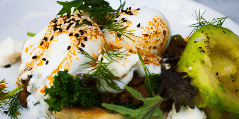 Eggs Benedict with Avocado and Herbs on Ceramic Plate