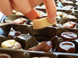Up close photo of a hand reaching into a box of chocolates from a candy store in Cleveland, Ohio and picking up a single piece of chocolate to try