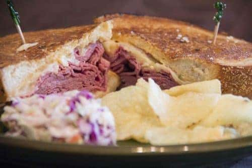 Reuben sandwich cut in half on plate next to chips and coleslaw