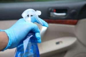 Person in a blue glove holding a spray bottle of cleaning spray at a car's interior door