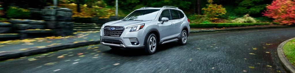 A silver Subaru SUV driving along a scenic road surrounded by trees with autumn foliage