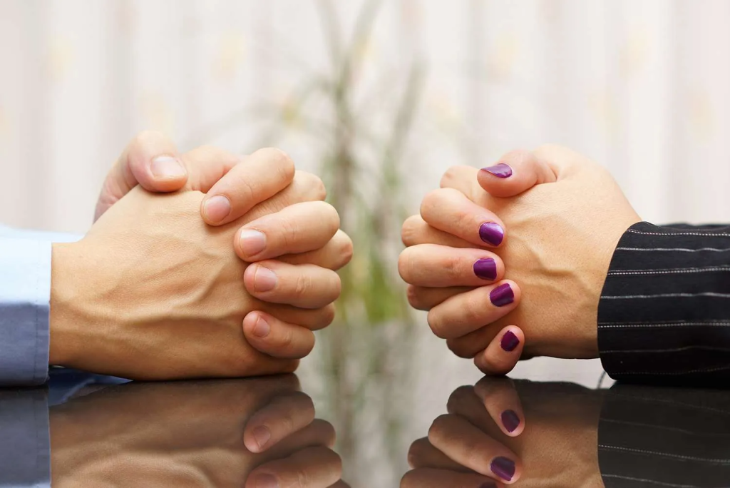 Two people sitting across from each other with hands clasped on a table