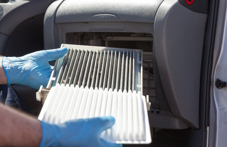 technician wearing gloves installing the air filter in a car