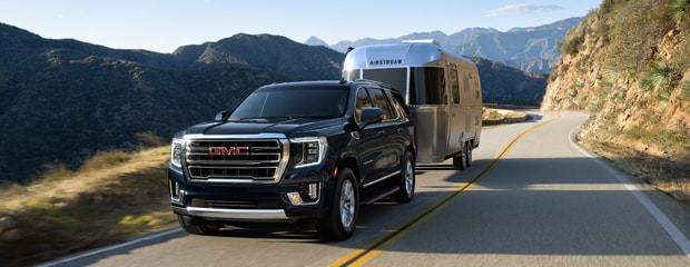 A 2023 GMC Yukon towing a camper on a scenic road, showcasing its powerful towing capability.