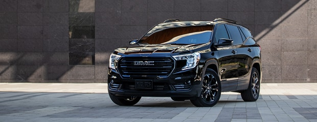A 2020 GMC Terrain driving along a winding mountain road surrounded by trees and rocky terrain.