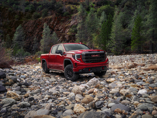 A 2023 GMC Sierra 1500 parked on a scenic mountain road surrounded by trees and rocky terrain.