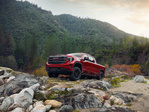 A 2023 GMC Sierra 1500 parked on a scenic mountain road surrounded by trees and rocky terrain.