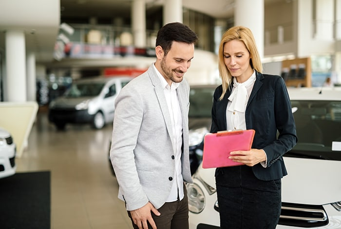 A smiling couple talks with a car salesman holding a tablet.