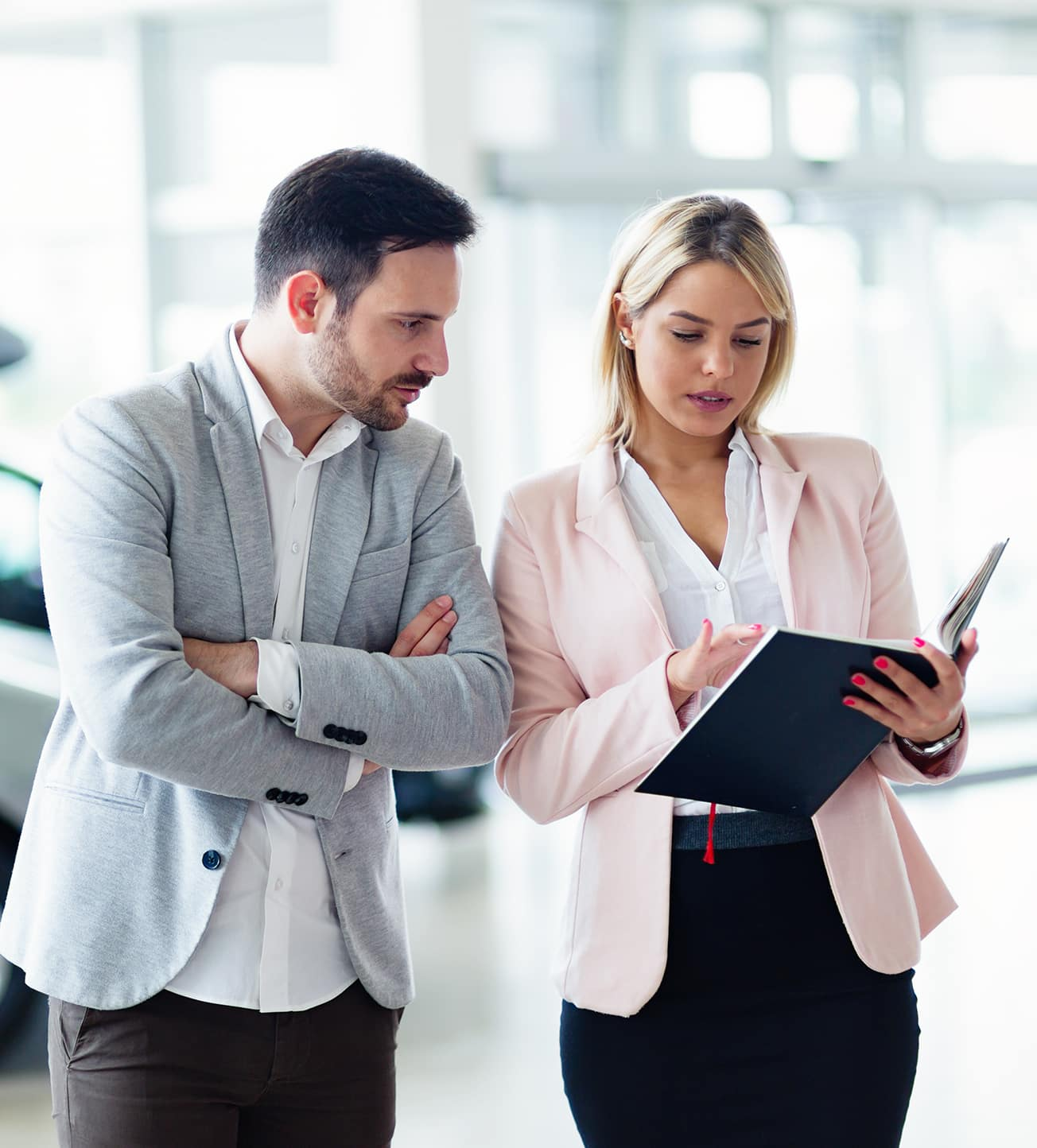 Man and woman looking at a white car in a bright dealership.