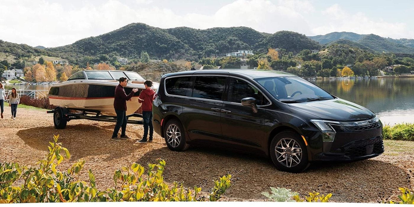 Black 2027 Chrysler Pacifica Limited towing a motorboat beside a lake, for sale at Ross Downing CDJR of Mobile, AL