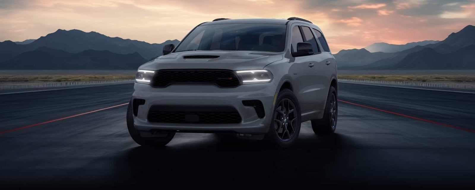 Gray 2026 Dodge Durango with its LED headlights lit on an open road at dusk; new Durango SUVs for sale at Ross Downing CDJR of Mobile, AL