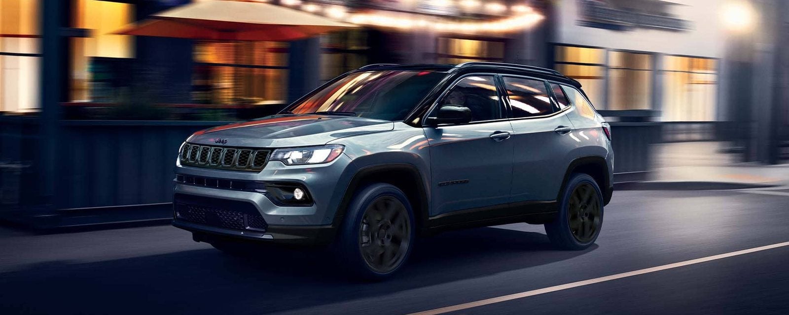 Gray 2026 Jeep Compass driving down a city street at dusk; new Jeep Compass SUVs for sale at Ross Downing CDJR of Mobile, AL