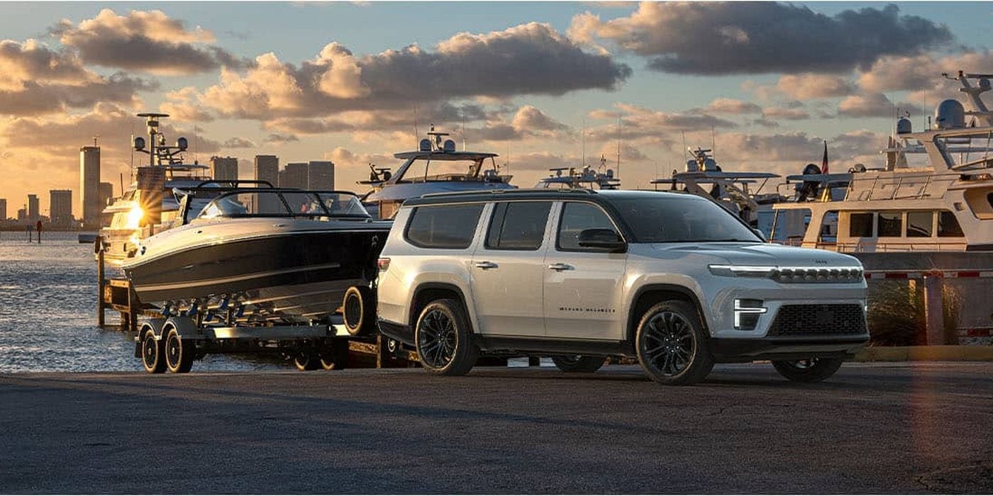 White 2026 Jeep Grand Wagoneer towing a boat on a trailer at a marina, for sale at Ross Downing CDJR of Mobile, AL
