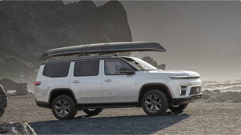 White 2026 Jeep Grand Wagoneer Upland with a canoe on its roof rack by a rocky shore; Grand Wagoneer financing at Ross Downing CDJR of Mobile, AL