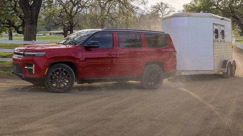Red 2027 Jeep Grand Wagoneer towing a horse trailer on a ranch road; trade in your vehicle at Ross Downing CDJR of Mobile, AL