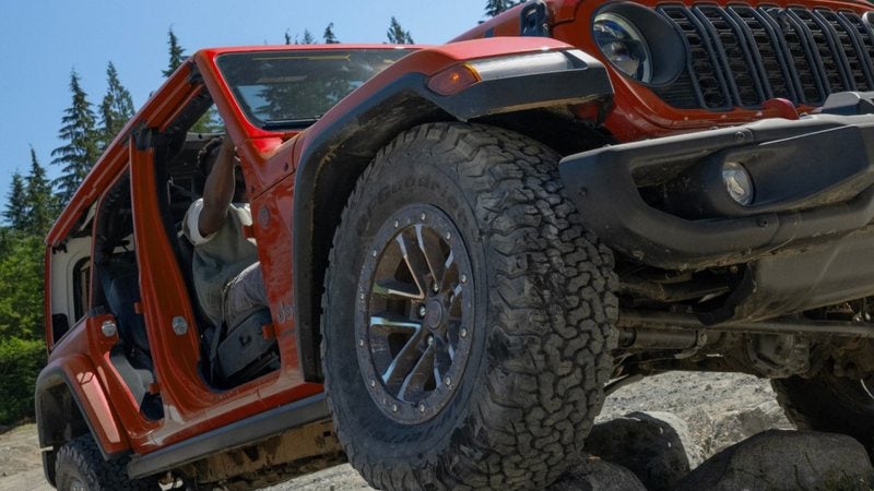 Red 2026 Jeep Wrangler with the doors off climbing rocks; Wrangler financing at Ross Downing CDJR of Mobile, AL