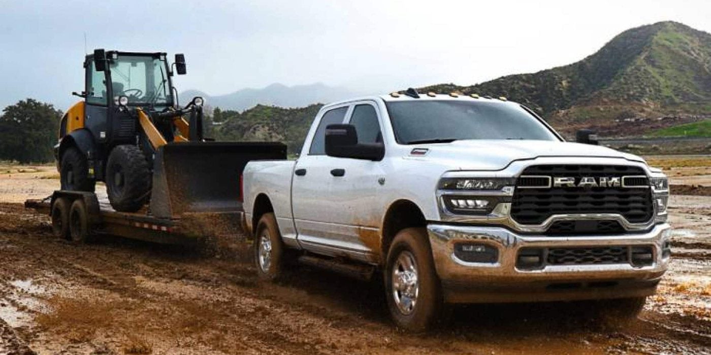 White 2027 Ram 2500 Crew Cab towing a wheel loader on a trailer through mud, for sale at Ross Downing CDJR of Mobile, AL