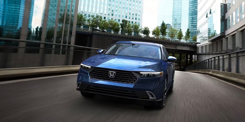 Blue Honda sedan driving through a modern city corridor, photographed from the front with motion blur on the road.