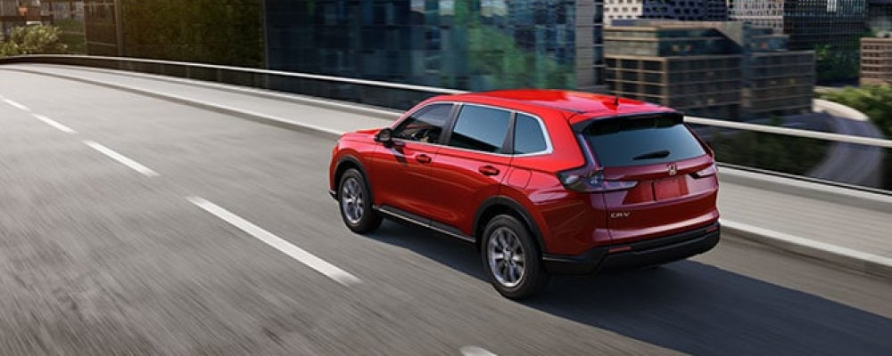 Red Honda CR-V driving on an elevated city roadway, shown from the rear three-quarter angle with motion blur.