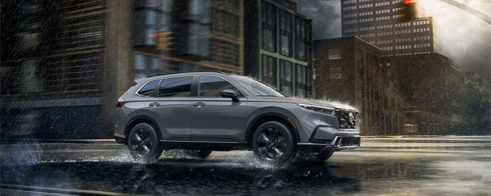2024 Honda CR-V driving through a rain-soaked city street, with water splashing from the tires and buildings in the background.