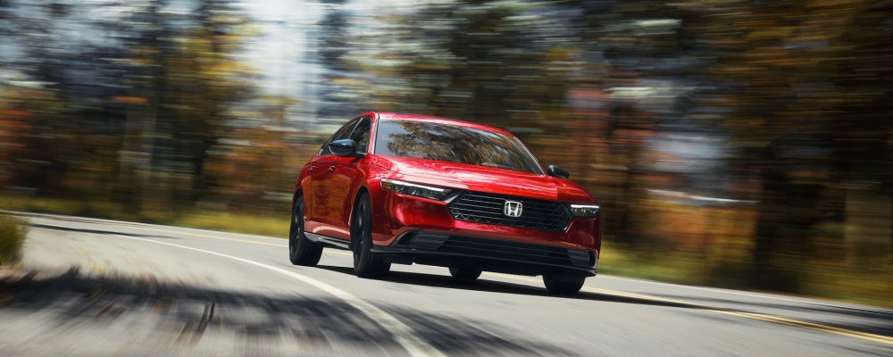 Red Honda sedan traveling along a roadway, photographed from a low angle with motion blur in the surroundings.
