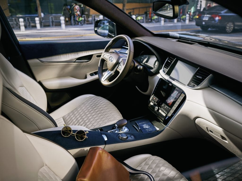 The interior of a white and navy blue car INFINITI QX50. A passport is visible in the center console.