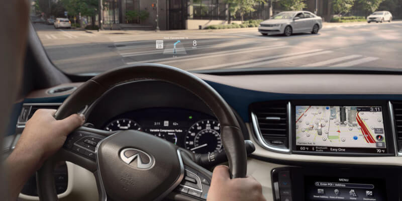 Driver’s view from inside a car Infiniti QX50 navigating a city intersection, with navigation data displayed on the windshield and dashboard.