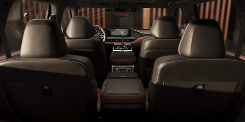 Dark interior of a car INFINITI QX80, showing the backs of two front seats and two second-row seats, with a center console.